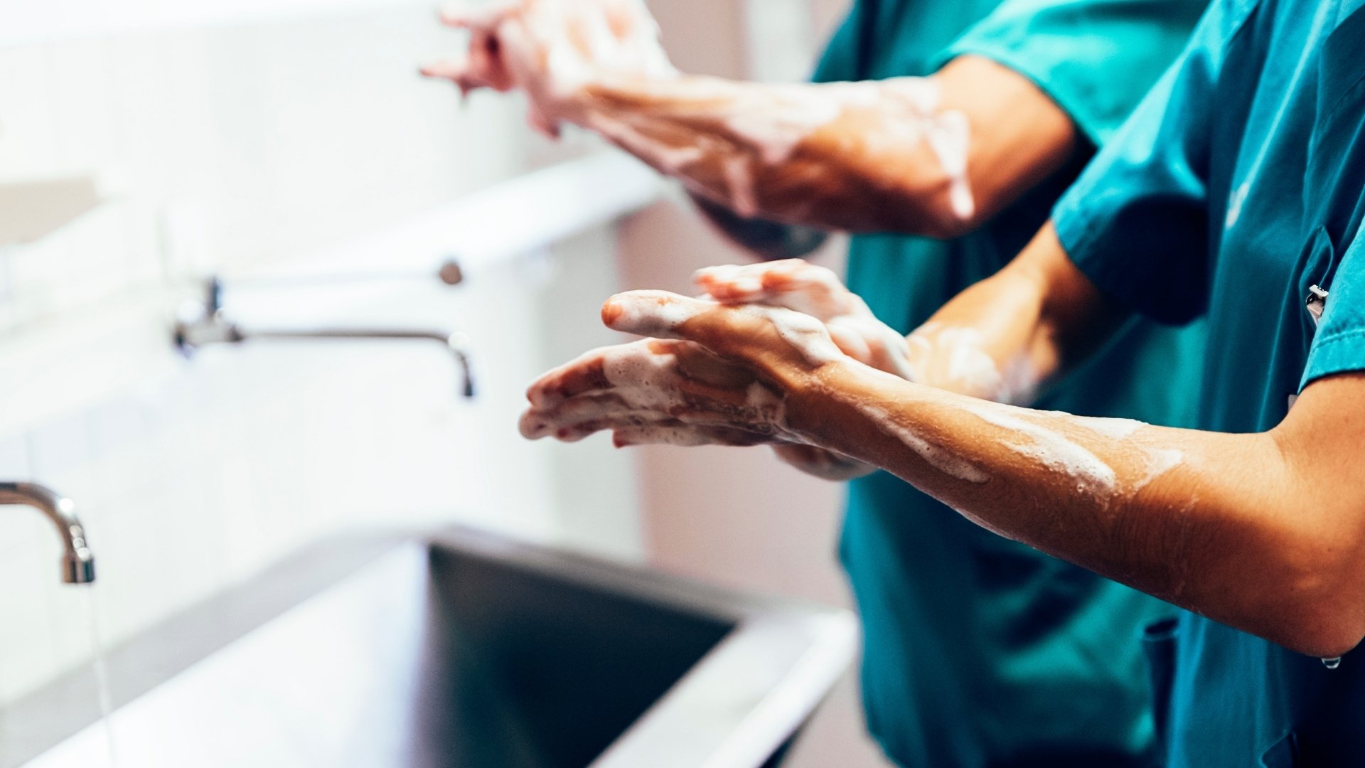 Vårdpersonal tvättar händerna noggrant vid ett handfat i vårdmiljö. Bilden visar en viktig hygienrutin för att förebygga smittspridning och skydda patienter och personal.