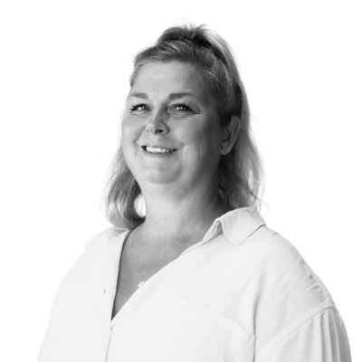 Porträttfoto i svartvitt av Jenny Samuelsson, utbildningsledare. En kvinna med axellångt blont hår och ljus skjorta, som ler mot kameran.