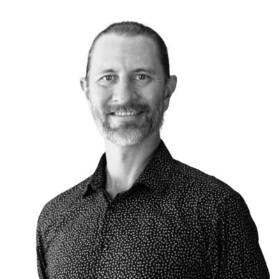 Porträttfoto av Andres Bergström. Han är utbildningsledare på Vårdyrkeshögskolan och ler mot kameran. Bilden är svartvit och tagen mot en ljus bakgrund. Han bär en mörk, mönstrad skjorta och har en avslappnad hållning.